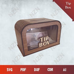 Puede incluir: Una caja de propinas de madera con un panel frontal transparente, que muestra un billete y las palabras "TIP BOX" en 3D. La caja tiene una ranura en la parte superior para insertar propinas. El diseño incluye el texto "Tip Box" en una pancarta roja.
