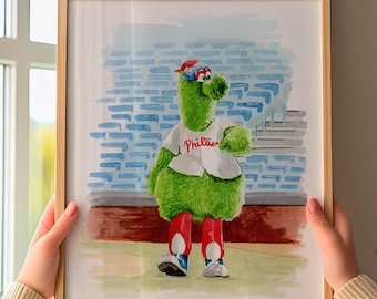 Può includere: Una stampa ad acquerello incorniciata raffigurante la mascotte verde Phillie Phanatic che indossa una maglia da baseball bianca con la scritta Phillies in corsivo rosso, un berretto rosso e pantaloni rossi, davanti a un muro di mattoni blu.