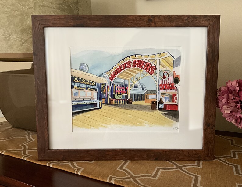 May include: A watercolor painting of a boardwalk scene with a red and white sign that reads "Doddys Piers". The painting features a blue and white building with the text "La Bakerie, Funnel Cakes" and other shops and buildings in the background.