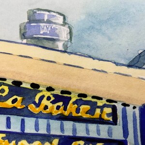 May include: A watercolor painting of a building with a sign that reads "La Baguette". The building is painted in shades of blue and yellow, with a white roof. The sign is painted in gold lettering.