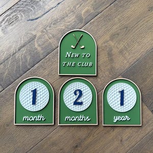 May include: Four arch-shaped wooden signs with a green background and light wood trim. One sign features two crossed golf clubs and the text New to the club. Three signs feature a white golf ball graphic with the numbers 1, 2, and 1, and the text month, months, and year.