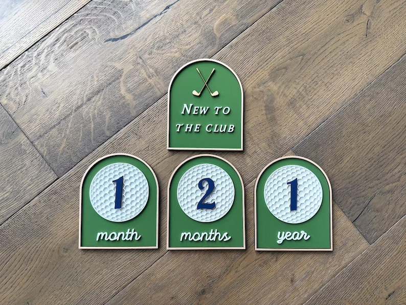 May include: Four arch-shaped wooden signs with a green background and light wood trim. One sign features two crossed golf clubs and the text New to the club. Three signs feature a white golf ball graphic with the numbers 1, 2, and 1, and the text month, months, and year.