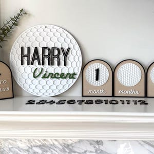 May include: A circular white golf ball textured sign with the black text HARRY and green text Vincent, alongside three arched signs with golf ball textures, black numbers, and the text New to the club, month, months, year, plus loose black numbers.