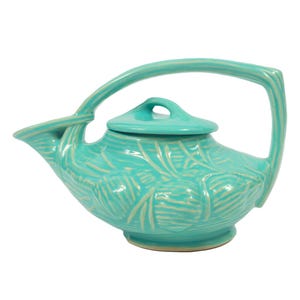 May include: A turquoise ceramic teapot featuring a raised relief pattern of pinecones and needles. The teapot has a single arched handle that connects to the spout and a removable lid with a small handle on top, all in a glossy finish.
