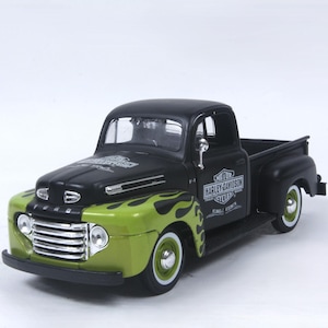 May include: A die-cast model of a vintage Ford pickup truck featuring a matte black body with lime green front fenders adorned with black flame graphics. The doors display the Harley-Davidson logo, and the front grille is finished in chrome.