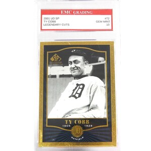 Puede incluir: Tarjeta de béisbol de Ty Cobb con uniforme de los Tigres de Detroit, calificada por EMC Grading. La tarjeta, con borde dorado, se titula "Legendary Cuts". El texto "1905-1928 OUTFIELD" está en la parte inferior.