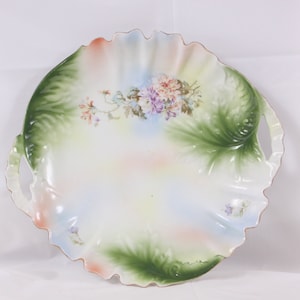 May include: A white porcelain serving platter with green and pink floral designs and two handles. The platter has a scalloped edge.