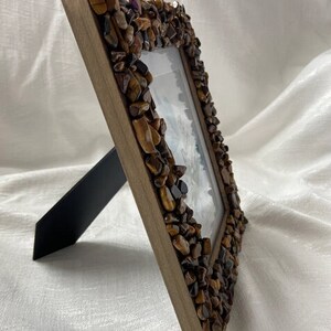 Könnte beinhalten: Ein brauner Holzbilderrahmen mit Ständer. Der Rahmen ist mit kleinen braunen und goldenen Steinen verziert.