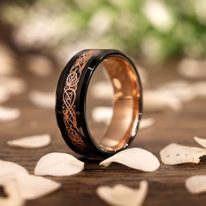 May include: A black tungsten carbide ring with a rose gold Celtic knot design.
