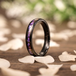 Könnte beinhalten: Ein schwarzer Ring aus Wolframcarbid mit einem dünnen Band aus schimmerndem lila und pinkfarbenem Glitzer, das in das Metall eingebettet ist.