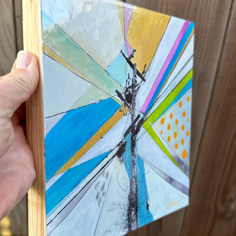 May include: Abstract painting on a wooden canvas with a geometric design featuring a central pole with lines radiating outward. The colors include blue, green, yellow, pink, and orange.