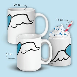 May include: Three white ceramic mugs with a blue heart and black wing design. The mugs are 11 oz, 15 oz, and 20 oz.