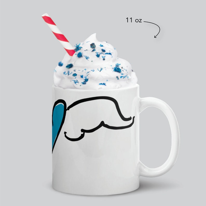 May include: White ceramic mug with a black line drawing of an elephant with a blue heart. The mug is filled with whipped cream and blue sprinkles. A red and white striped straw is in the mug. The mug is 11 oz.