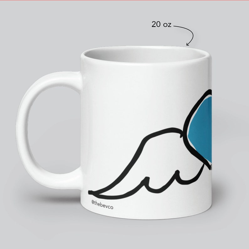May include: White ceramic mug with a black and blue wing design. The mug is 20 ounces and has the text "@thebevco" on the bottom.