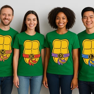 May include: Four people wearing green t-shirts with a yellow turtle shell design. Each shirt has a different colored belt and initial: M, R, D, and L. The shirts are paired with blue jeans.