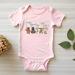 May include: Pink baby onesie with a graphic of Star Wars characters holding signs that say "The Force is Strong with This One".