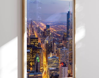 May include: An aerial view of a city skyline at dusk. The buildings are illuminated with warm lights, and the streets below are filled with traffic. The image is framed in a wooden frame.
