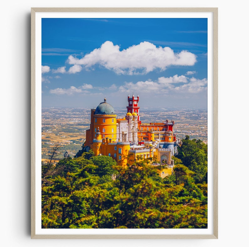 May include: A yellow and red castle with a blue domed roof sits on a hilltop overlooking a green forest and a distant city. The sky is blue with a large white cloud.