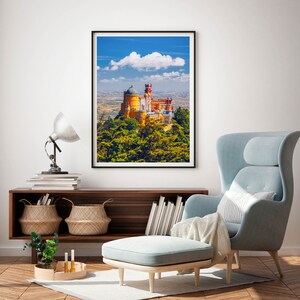 May include: A framed photograph of a yellow and red castle with a blue sky and white clouds in the background. The castle is surrounded by green trees.