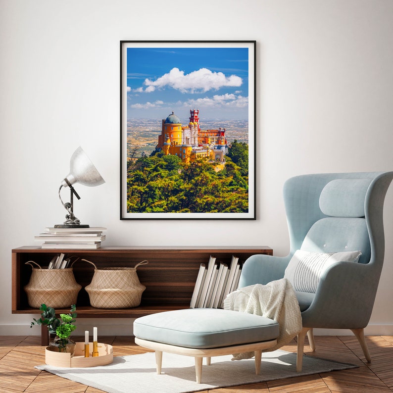 May include: A framed photograph of a yellow and red castle with a blue sky and white clouds in the background. The castle is surrounded by green trees.