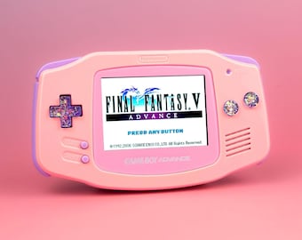 May include: A light pink and lavender Game Boy Advance handheld console featuring a screen displaying the Final Fantasy V Advance title screen with the text Press Any Button. The D-pad and action buttons have a glittery, multi-colored finish.