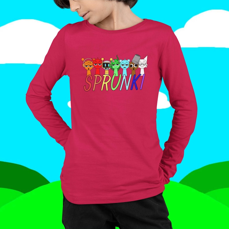 Puede incluir: Una camiseta roja de manga larga con la palabra "SPRUNKI" en letras coloridas. Encima de la palabra hay siete personajes de dibujos animados en varios colores y dise&ntilde;os. La camiseta est&aacute; hecha de un material suave.