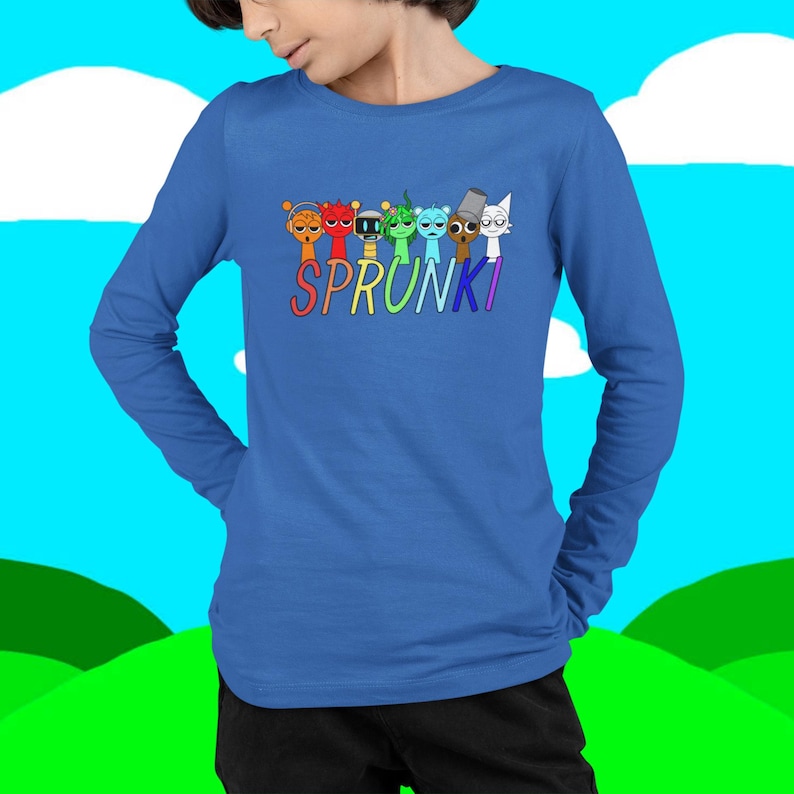 Puede incluir: Una camiseta azul de manga larga con la palabra "SPRUNKI" en letras coloridas. Encima de la palabra hay siete personajes de dibujos animados de varios colores. La camiseta es de un material suave.