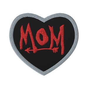 May include: Red embroidered heart-shaped patch with the word "MOM" and an arrow through the "O".
