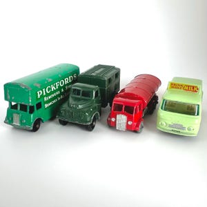 May include: A collection of four vintage die-cast toy trucks. The set includes a green Pickfords removal van, a dark green box truck, a red tanker truck, and a light green milk delivery truck with the text Drink More Milk on the roof sign.