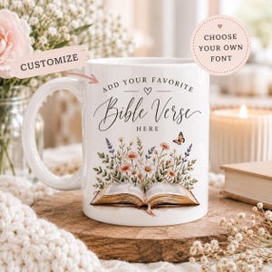 Peut inclure: Un mug en céramique blanche orné d'un dessin représentant un livre ouvert avec un bouquet de fleurs sauvages et un petit papillon. Le texte indique ADD YOUR FAVORITE BIBLE VERSE HERE. Une étiquette rose au-dessus du mug indique CUSTOMIZE.