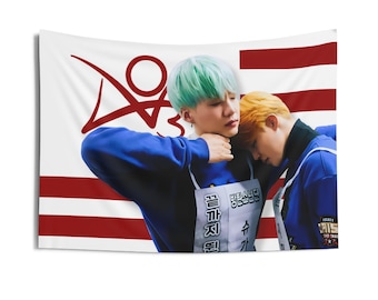 May include: A white wall tapestry with a red and white striped design and a red graphic. The tapestry features two people wearing blue tops, one with mint green hair and the other with orange hair. Text is visible on the tapestry.