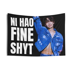 以下が含まれることがあります： 「Ni Hao Fine Shyt」と白文字で書かれた黒い旗。青いデニムジャケットを着た人が旗に描かれている。
