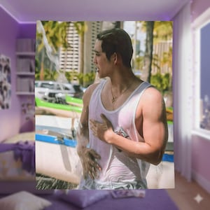 May include: A white tank top with a small floral design is worn by a person. The person is wet, with water streaming down their body. A gold necklace with a cross pendant is visible. The background includes palm trees and a building.