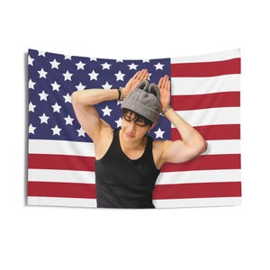 Könnte beinhalten: Eine Person mit einer grauen Mütze und einem schwarzen Tanktop posiert vor einer amerikanischen Flagge.