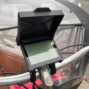 May include: A black bike handlebar mount with a screen attached. The screen is in a protective case with a clear cover. The mount is attached to a silver handlebar.