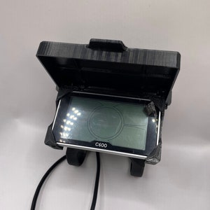 Könnte beinhalten: Ein schwarzes und silbernes E-Bike-Display mit einem Bildschirm, der einen Tachometer, den Batteriestand und andere Informationen anzeigt. Das Display ist mit "C600" beschriftet.