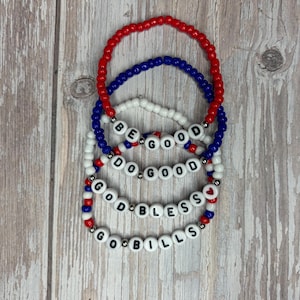 May include: Four beaded bracelets in red, white, and blue. The bracelets have white letter beads spelling out "BE GOOD", "DO GOOD", "GOD BLESS", and "GO BILLS". The bracelets are on a light wood grain surface.