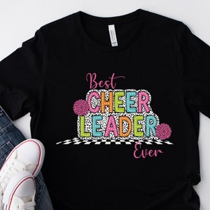 May include: Black t-shirt with the text "Best Cheer Leader Ever" in colorful letters with a checkered pattern and pom-poms.