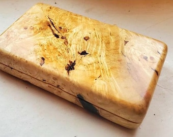 May include: A rectangular wooden box with a polished, light tan finish featuring a prominent natural burl wood grain pattern. The surface displays swirling golden-yellow tones, dark brown organic inclusions, and a smooth, glossy texture.