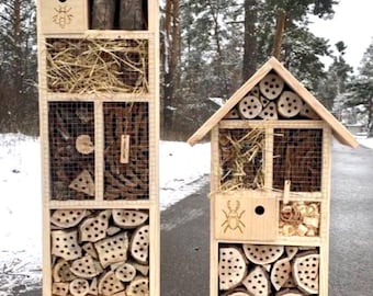 May include: Two tall wooden insect hotels with gabled roofs, featuring multiple compartments filled with drilled logs, straw, twigs, and bricks. The left structure has a bee icon, while the right structure displays a beetle icon on the front panels.