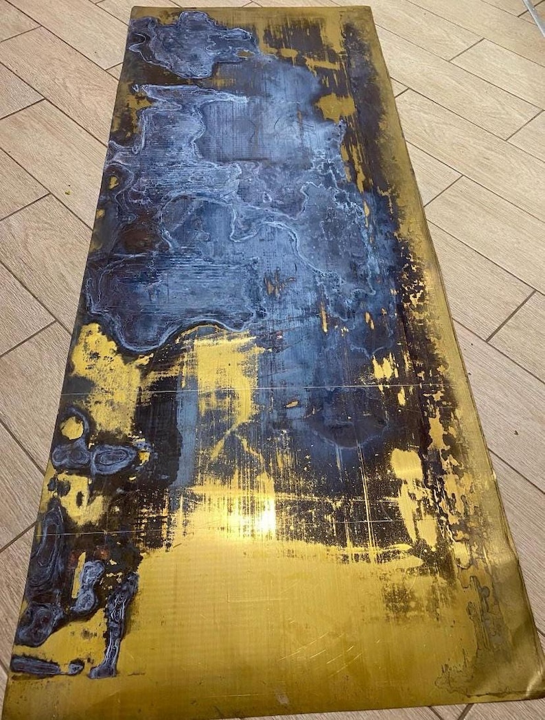 May include: A rectangular table top with a distressed finish. The surface features a blend of gold, navy blue, and black hues, creating a unique, abstract pattern. The gold areas have a metallic sheen, while the blue and black sections appear matte.