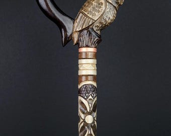 May include: A handcrafted wooden walking cane with a carved owl perched atop. The dark brown handle is shaped like a heart. The shaft features intricate floral and geometric patterns, with light brown and cream accents.