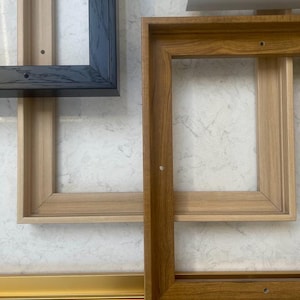 May include: Four different picture frames in various colours and styles. The frames are made of wood and metal. The frames are arranged in a stack, with the largest frame at the bottom and the smallest frame at the top.