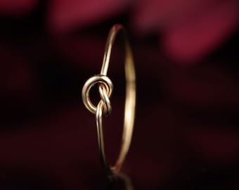 Puede incluir: Un anillo de nudo de oro simple. El anillo es delgado y delicado, con un diseño de nudo en el centro.