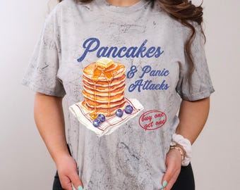 Może przedstawiać: Szary T-shirt z grafiką w stylu vintage przedstawiającą stos naleśników z syropem i masłem, borówkami i tekstem "Pancakes & Panic Attacks" oraz "buy one get one".