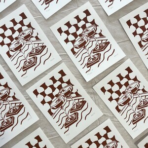 Puede incluir: Una colecci&oacute;n de grabados art&iacute;sticos en blanco y marr&oacute;n. Cada grabado presenta una ilustraci&oacute;n estilizada de copas de c&oacute;ctel, un patr&oacute;n de cuadros y l&iacute;neas onduladas. Los grabados est&aacute;n numerados y firmados, con el texto "AKM" visible.