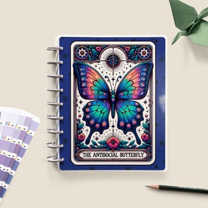 May include: A blue and white spiral bound notebook featuring a colourful butterfly illustration on the cover. The butterfly has iridescent wings with blue, green, and pink hues. The text "THE ANTISOCIAL BUTTERFLY" is printed below the butterfly.