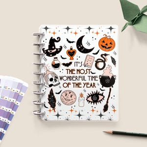Puede incluir: Una agenda blanca con temática de Halloween, con ilustraciones de un sombrero de bruja, calabaza, murciélagos y el texto "IT'S THE MOST WONDERFUL TIME OF THE YEAR". La agenda está encuadernada en espiral.
