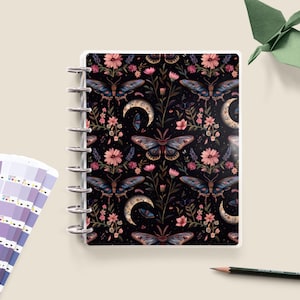 May include: A black and white planner with a floral and butterfly pattern. The planner has a clear cover and a silver coil binding.