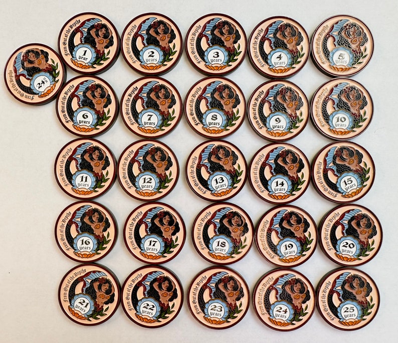 Op de afbeelding: Een verzameling ronde, houten tokens met een zeemeermin illustratie. Elke token heeft een nummer van 1 tot 25, met de tekst "From Out of the Depths" en "years" langs de rand. De tokens zijn bruin, beige en blauw.